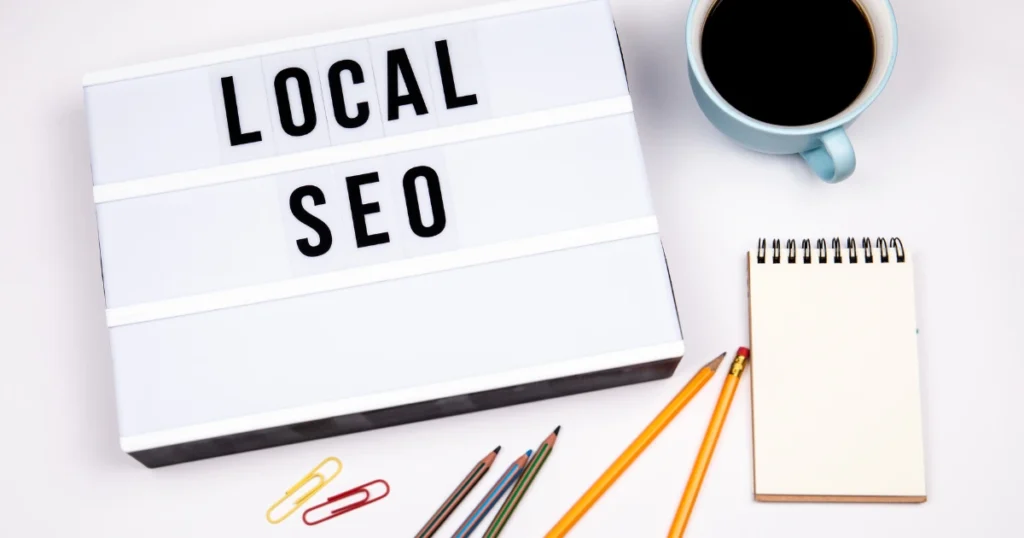 Top view of a workspace with a lightbox showing the words 'Local SEO', pencils, notebook, and a cup of coffee. Ideal for blog posts about local search engine optimization strategies or for Google Business Profile Optimization.